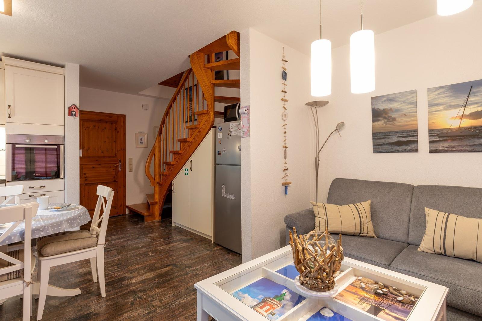 Wohn- und Essbereich mit Holztreppe, Sofa und Küchenzeile.