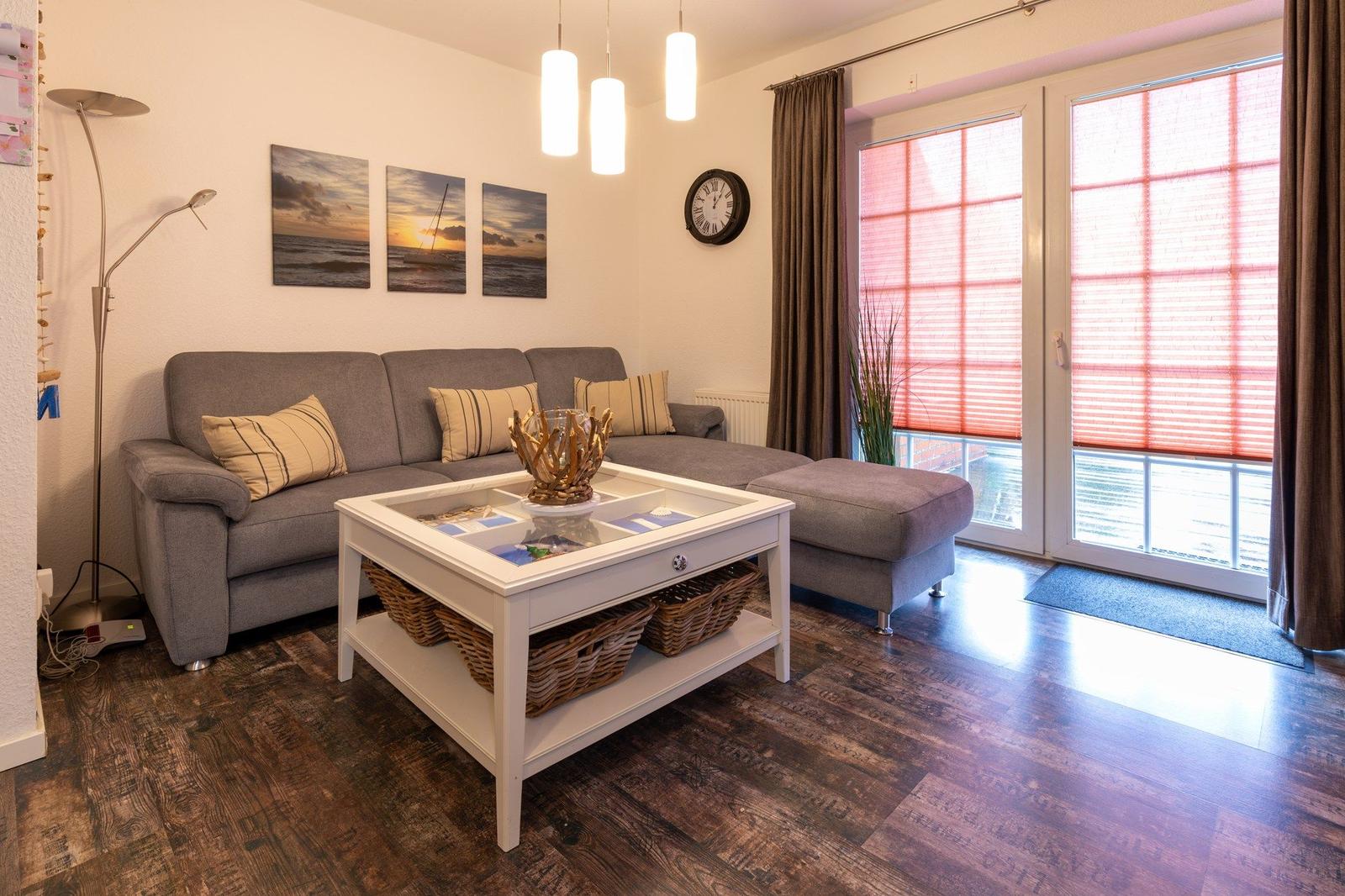 Wohnzimmer mit grauem Sofa, weißem Tisch und Holzboden.