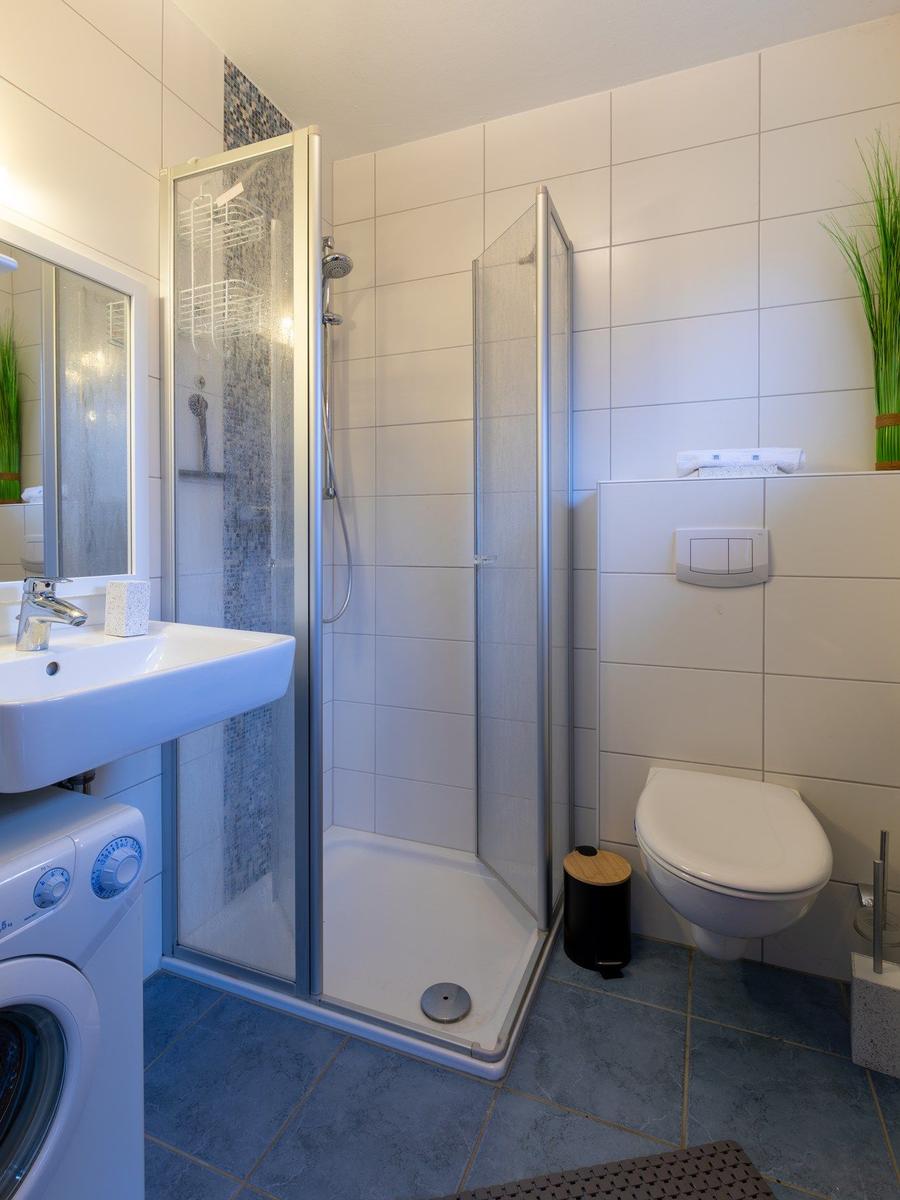 Badezimmer mit Dusche, Waschbecken und Toilette. Fliesenboden und Spiegelschrank.