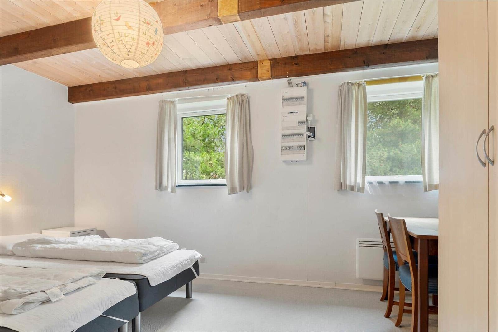 Zimmer mit Bett, Tisch, Fenstern und Holzdecke mit Balken.