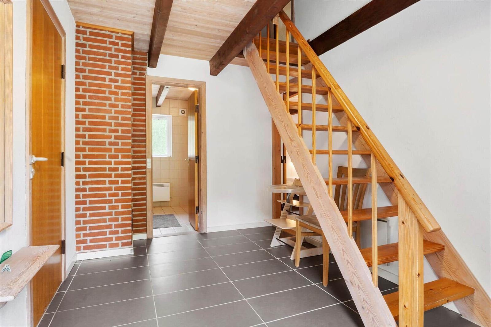 Holztreppe führt zur oberen Etage. Ziegelwand und Bodenfliesen sichtbar.