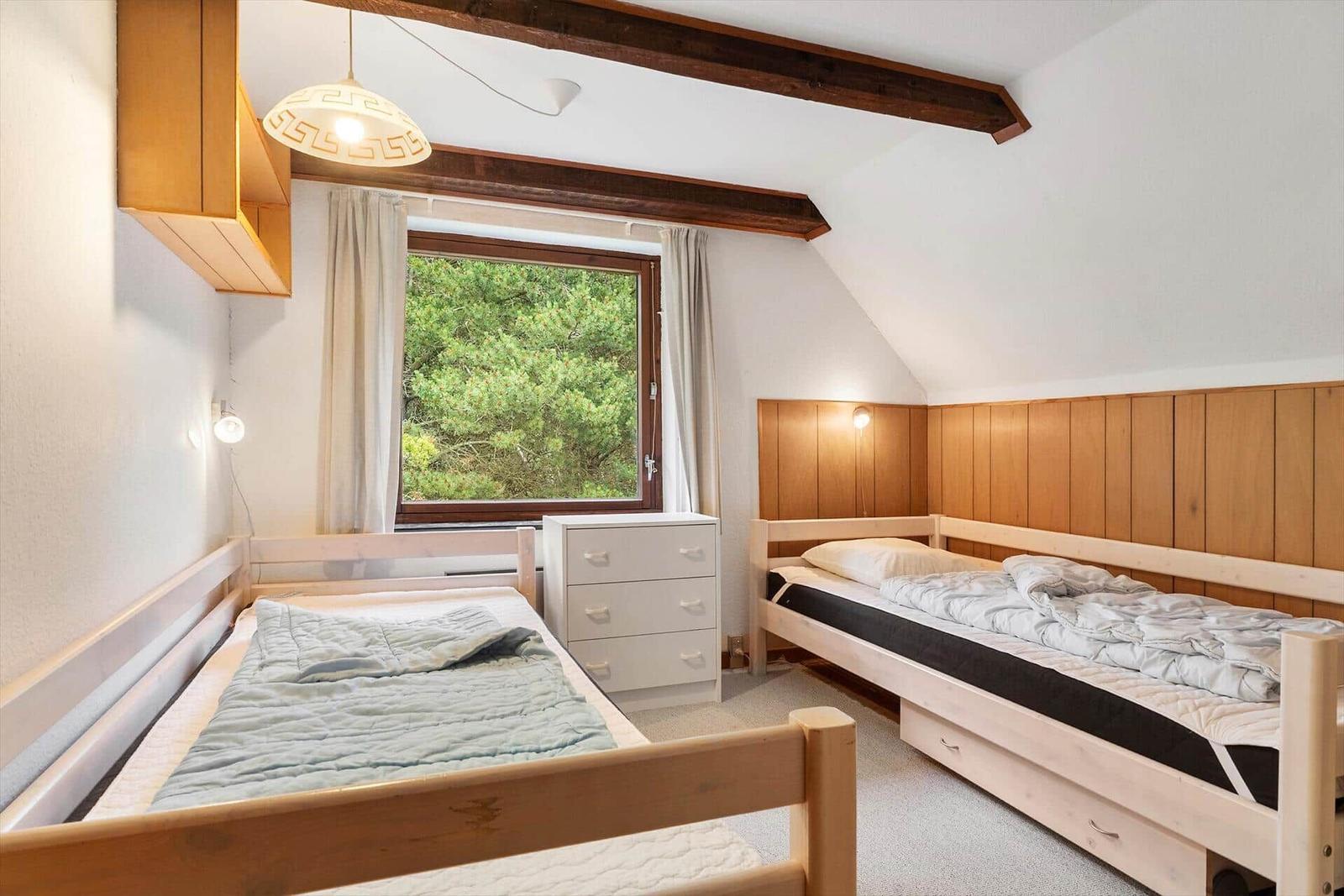 Zimmer mit zwei Betten, Holzwand und Fenster mit Blick auf Bäume.