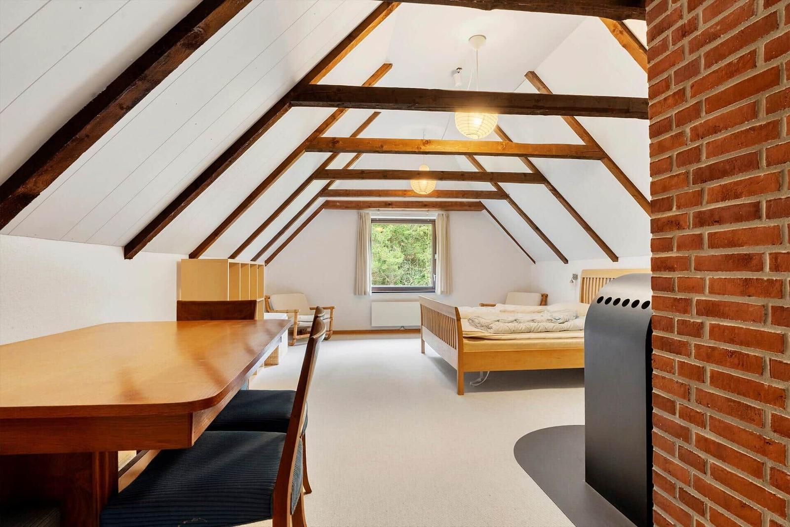 Dachgeschosszimmer mit Holzbalken, Bett, Tisch und Kaminwand.
