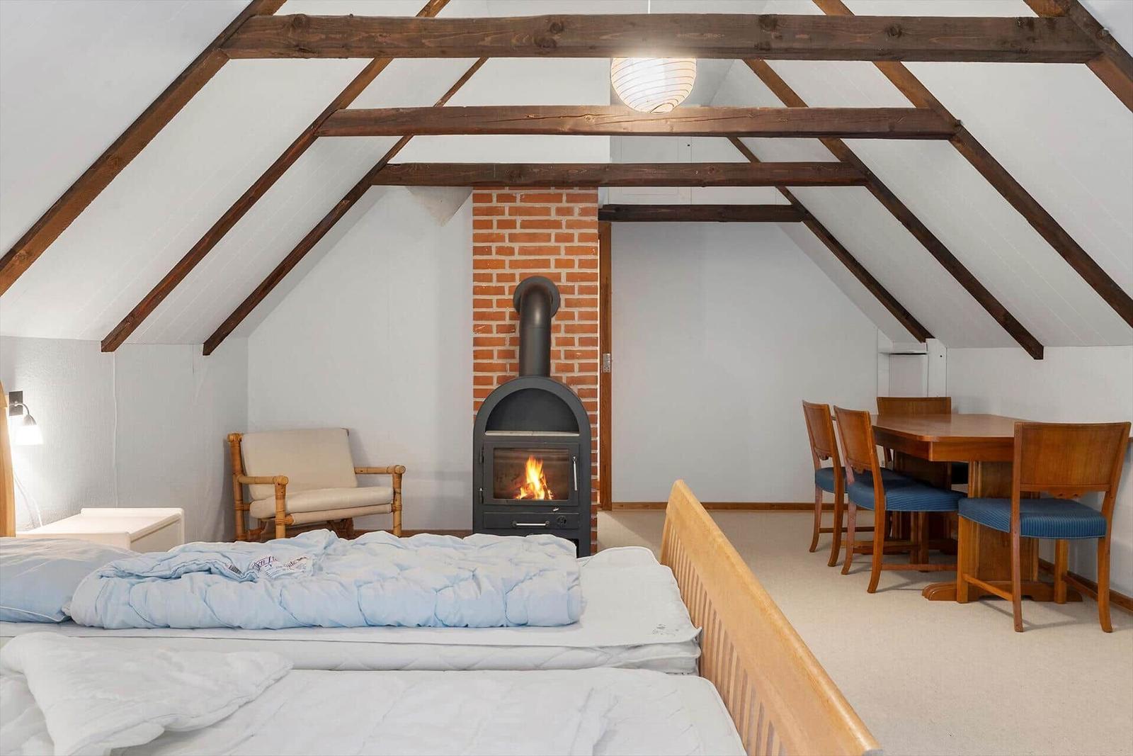 Schlafzimmer mit Kamin, Tisch und Stühlen unter Holzbalkendecke