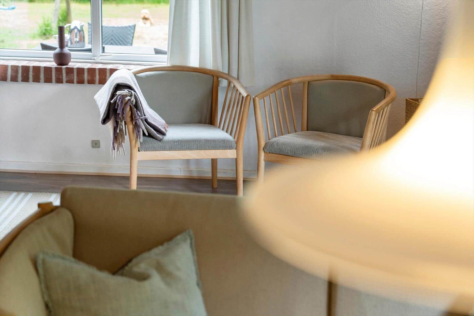 Zwei Holzstühle mit grauen Sitzkissen stehen vor einem Fenster mit Blick auf den Garten.