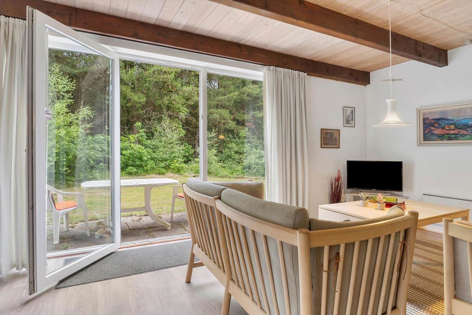 Wohnbereich mit Holzdecke, Glasfront und Gartenansicht.
