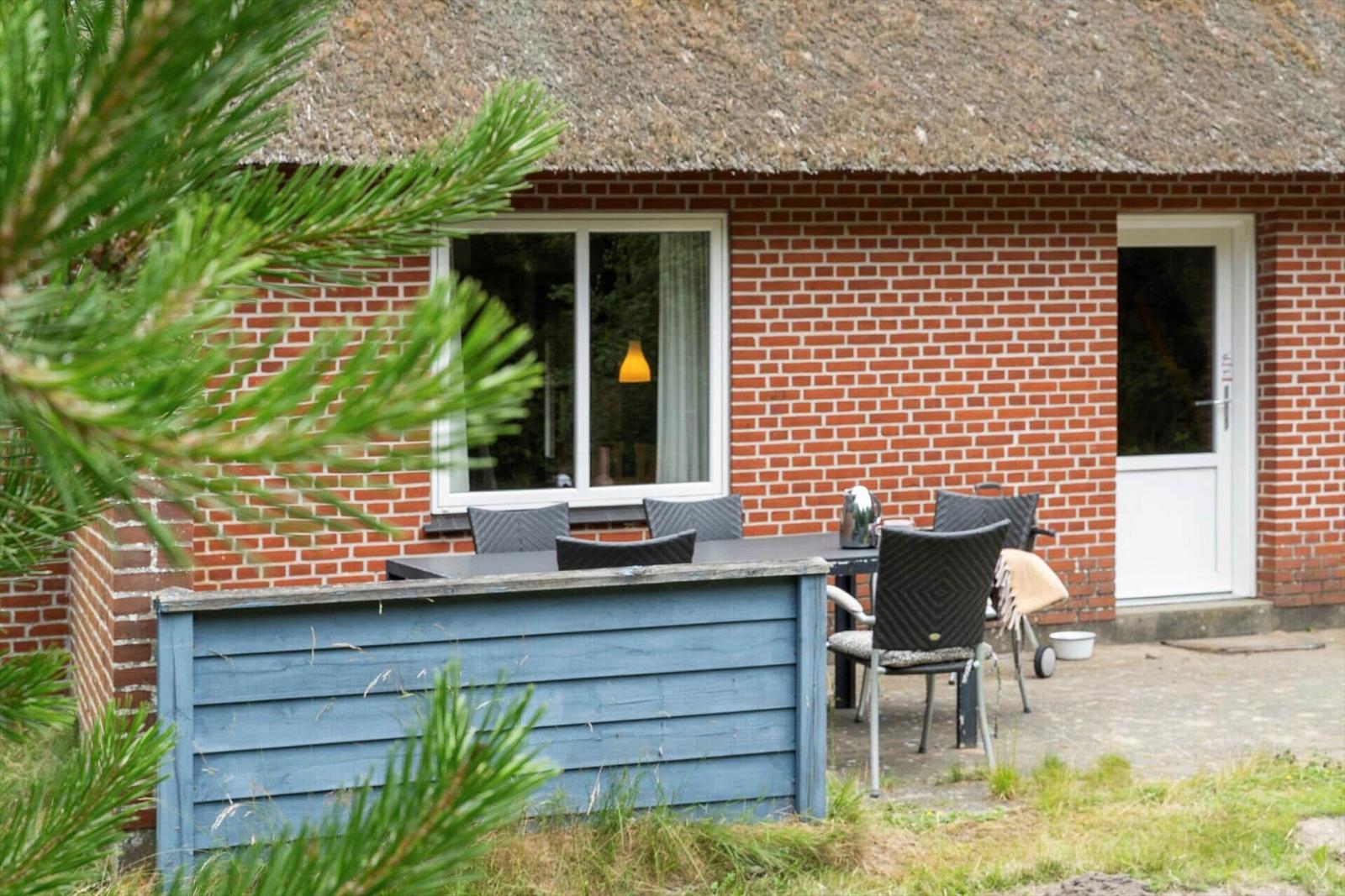 Rotes Backsteinhaus mit Strohdach und Außenbereich mit Tisch und Stühlen.