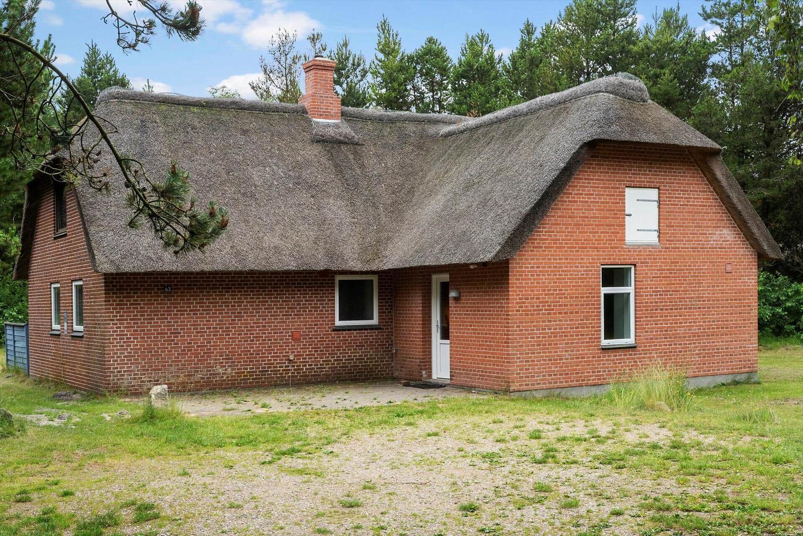 Rotes Backsteinhaus mit Strohdach und weißer Tür im Wald.