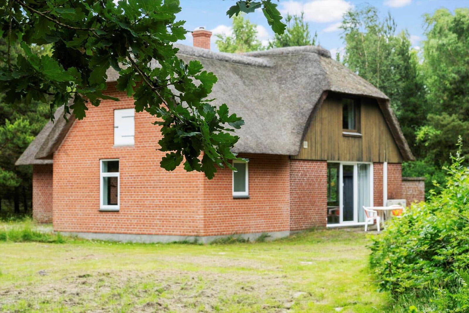 Haus mit strohgedecktem Dach und rotem Backstein. Gartenbereich mit Tisch und Stühlen.