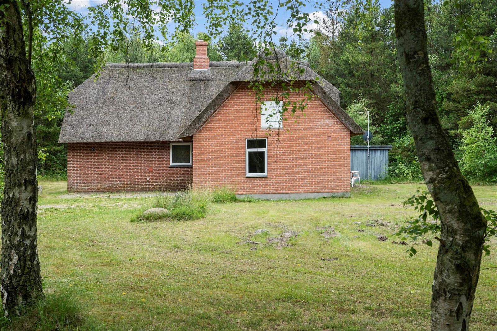 Rotes Backsteingebäude mit Strohdach und Fenstern im Grünen.
