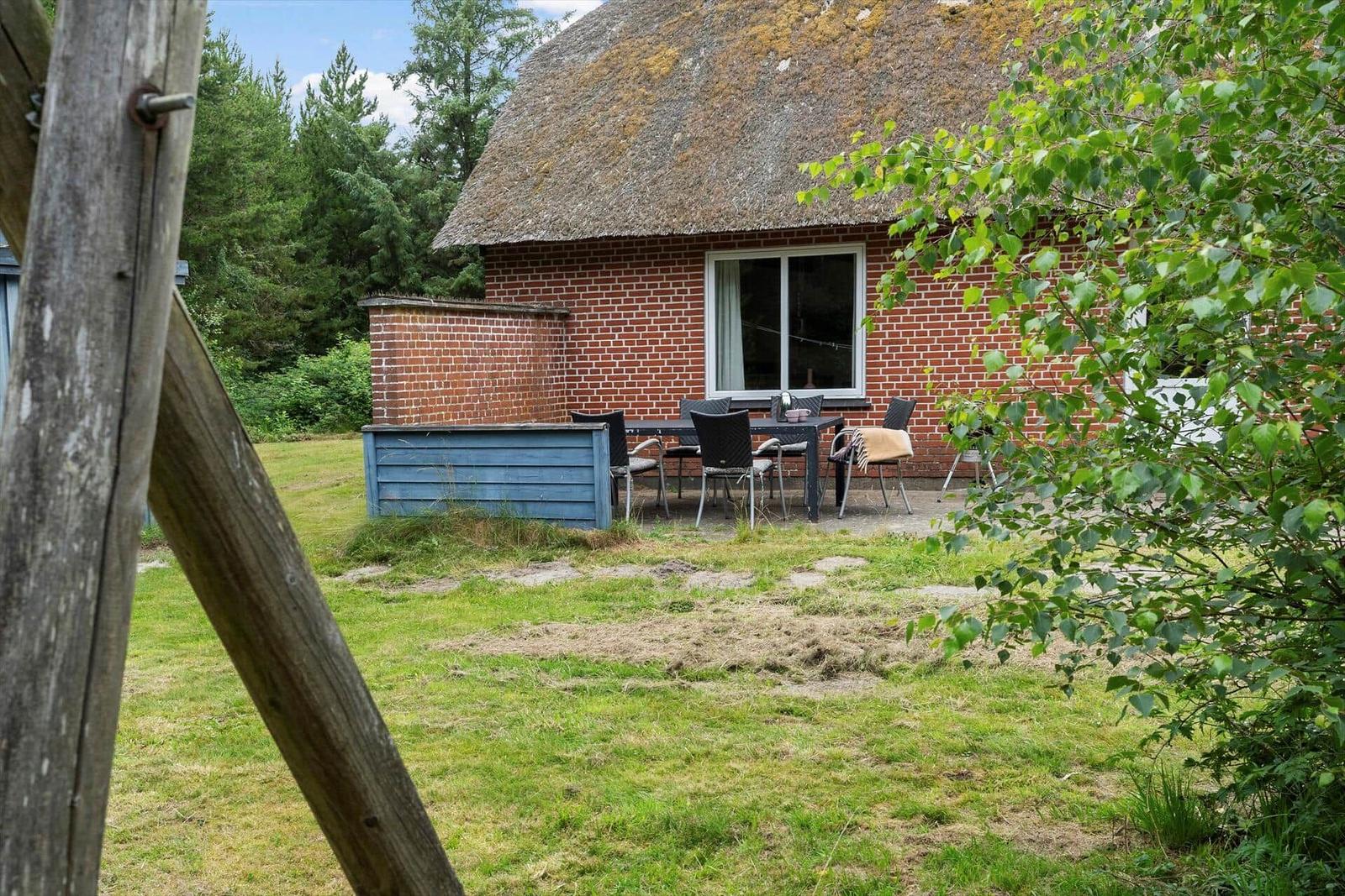 Rotes Backsteingebäude mit Strohdach und Gartenmöbeln. Grün umgeben mit Bäumen.