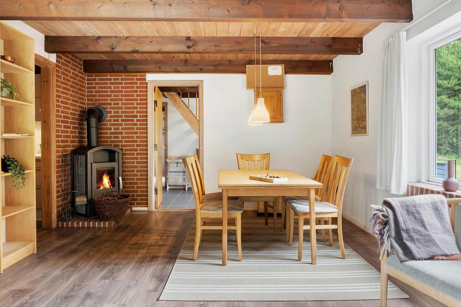 Esszimmer mit Holztisch, Stühlen und Kaminofen an Backsteinwand.