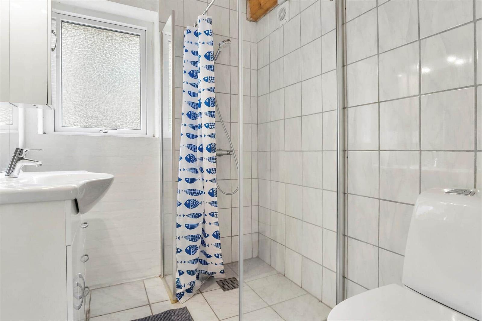 Badezimmer mit Dusche, Waschbecken und Toilette. Duschvorhang mit Fischmuster.