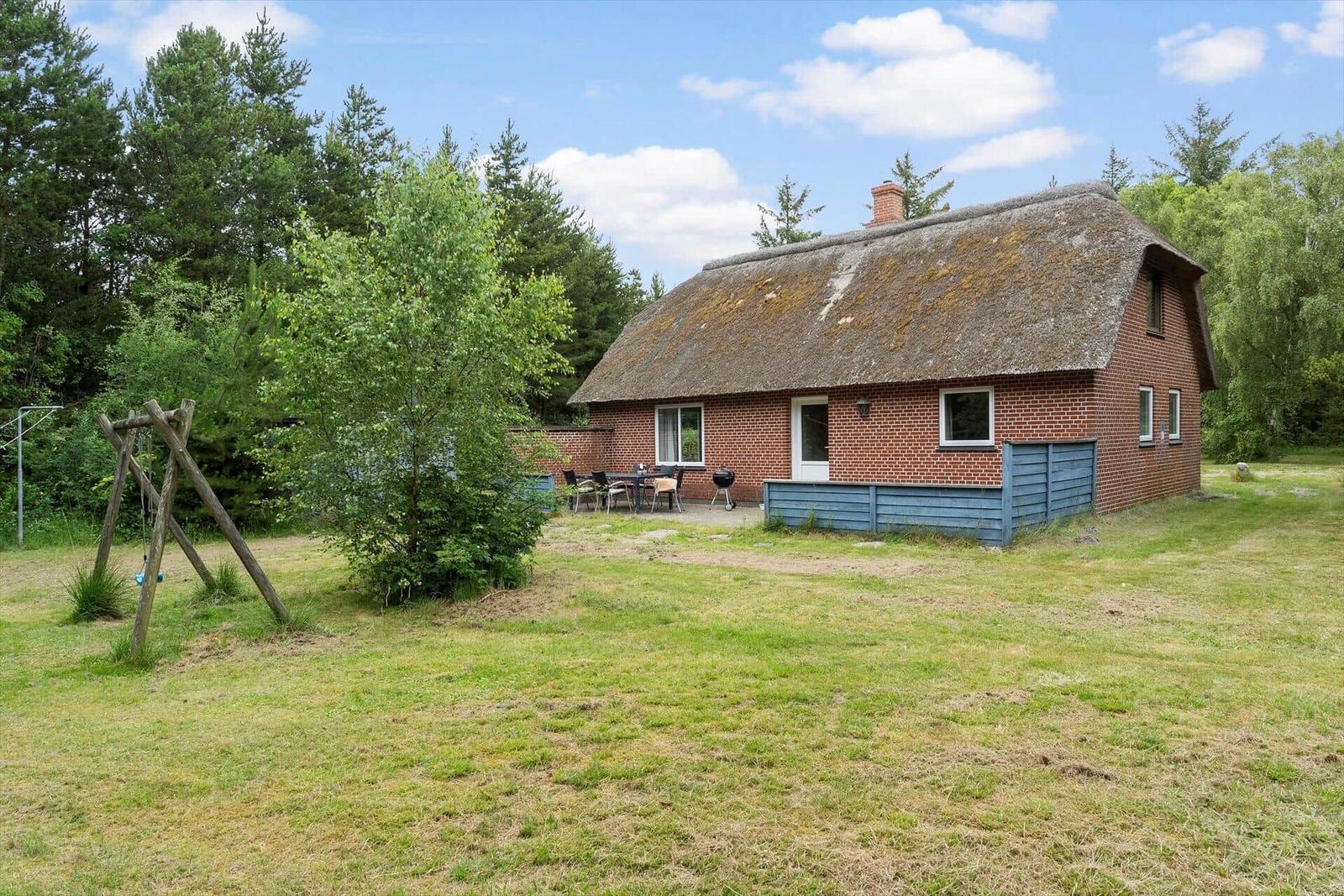 Rotes Backsteingebäude mit Strohdach, Garten und Grillplatz.