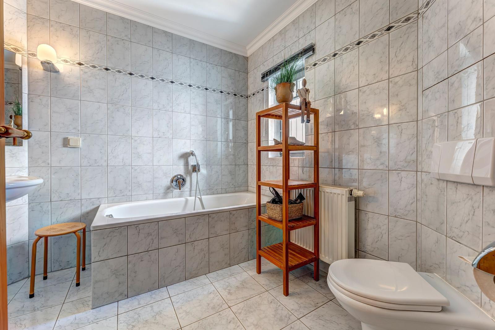 Badezimmer mit Badewanne, Toilette und Holzregal.