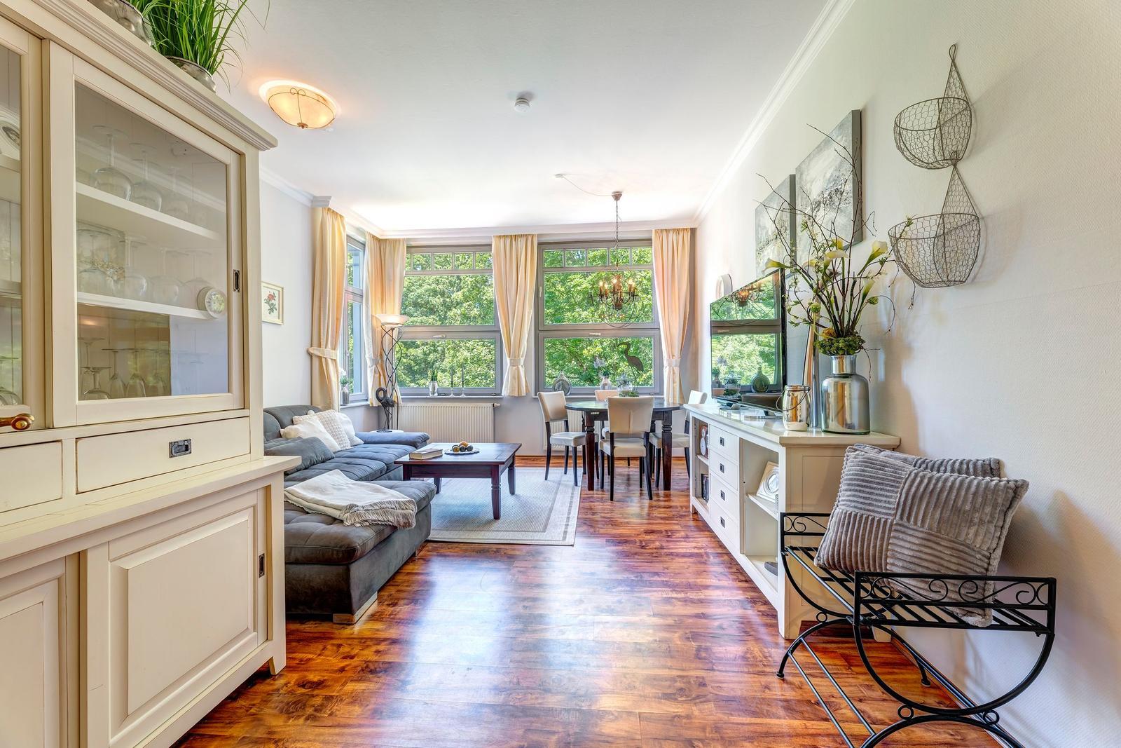 Wohn- und Essbereich mit Holzboden, Sofa, Tisch und Fenstern.