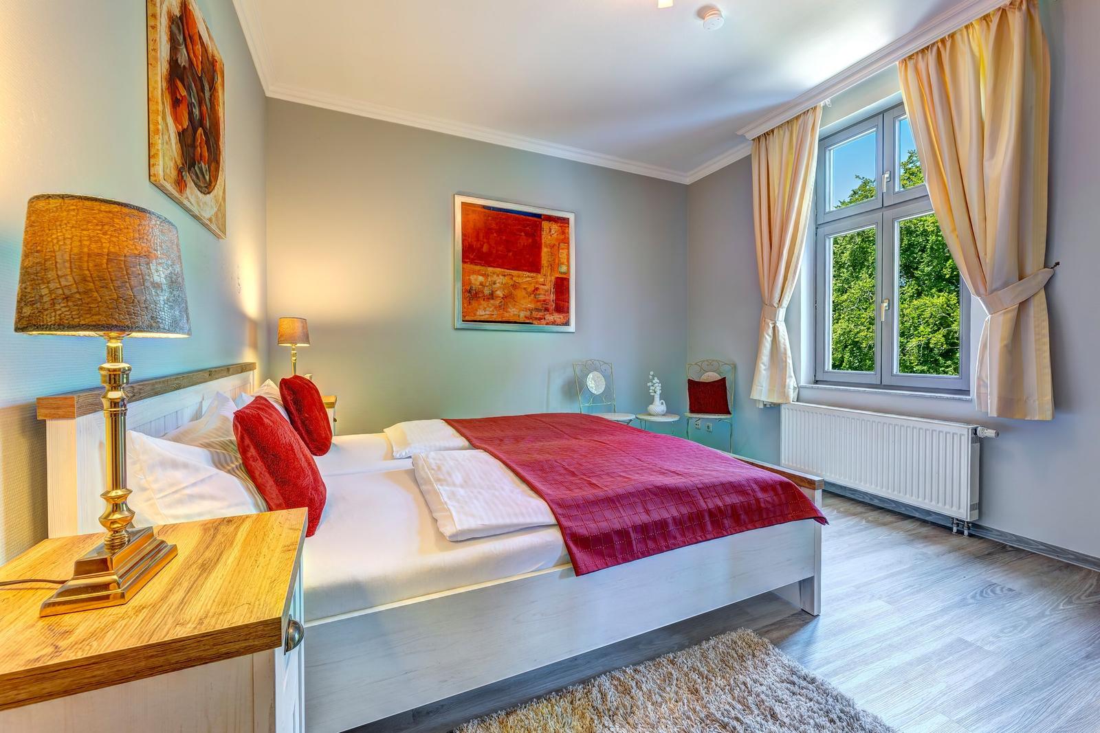 Schlafzimmer mit Bett, Fenster und Kunstwerken an den Wänden.