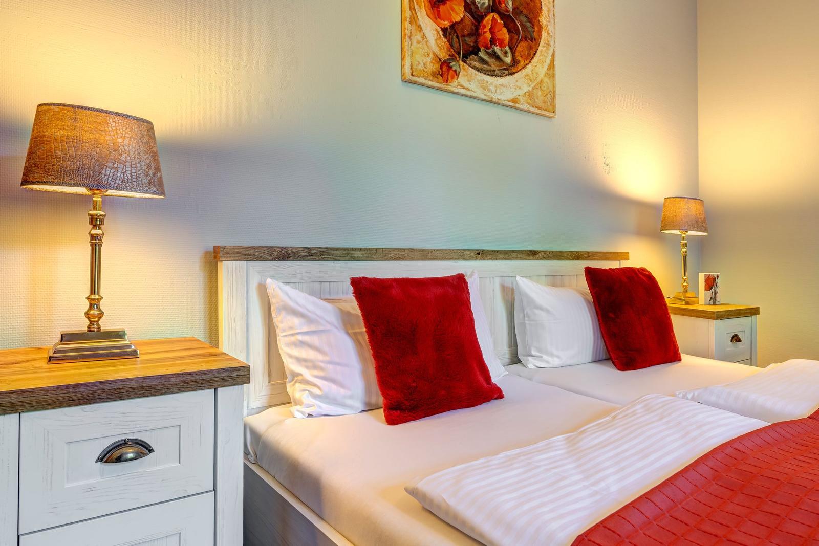 Schlafzimmer mit Bett, zwei Nachttischen und Lampen. Wandbild über dem Bett.