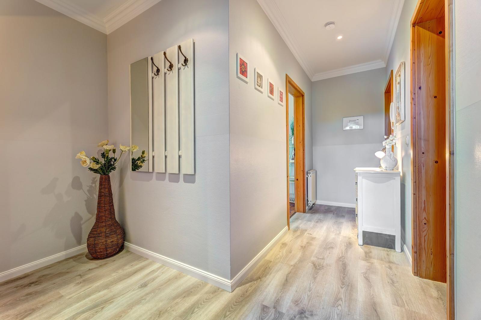 Flur mit Holzboden, Spiegelschrank und Vase mit Blumen.