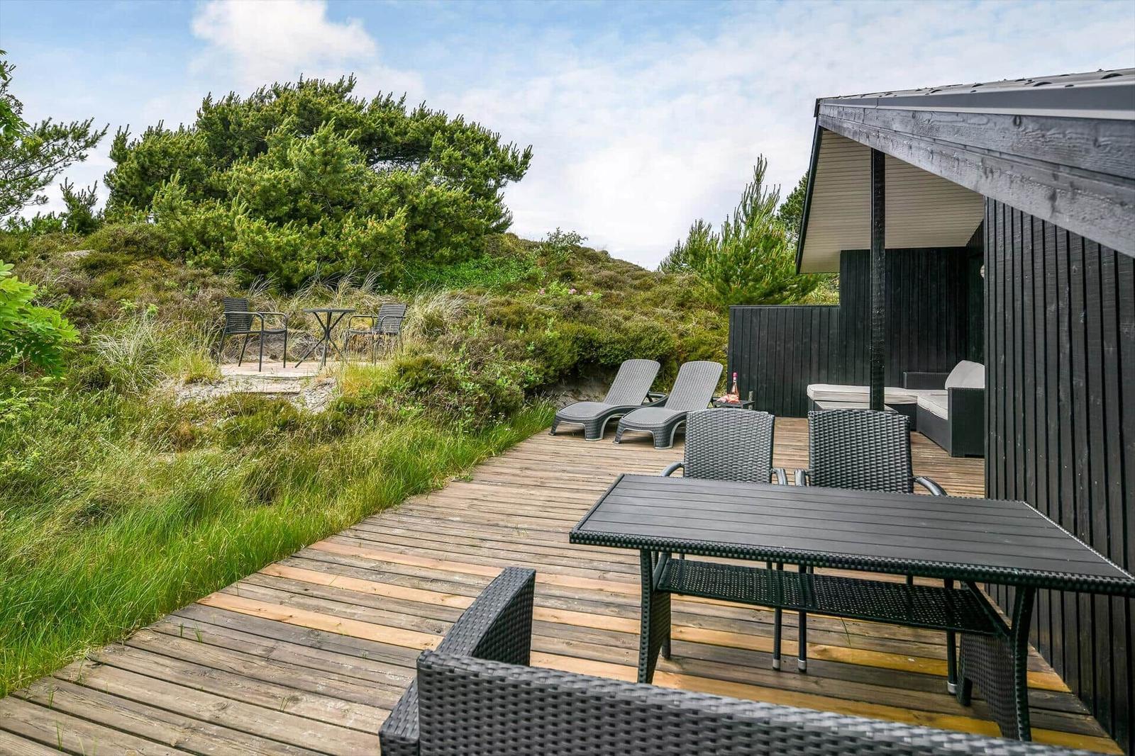 Terrasse mit Tisch, Stühlen und Liegen neben einem Holzhaus.