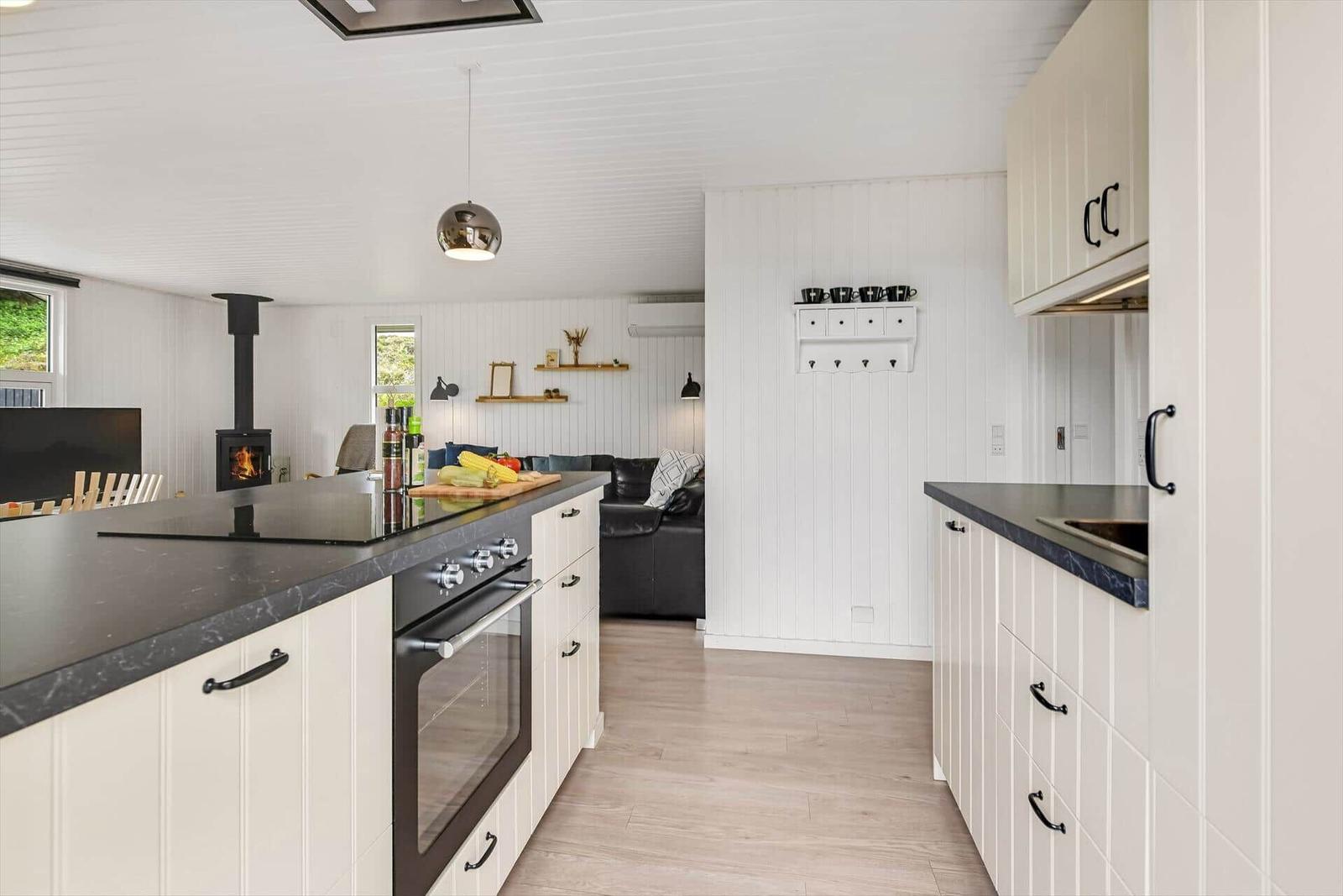 Küche mit Arbeitsplatte und Ofen. Im Hintergrund Wohnbereich mit Sofa und Kamin.