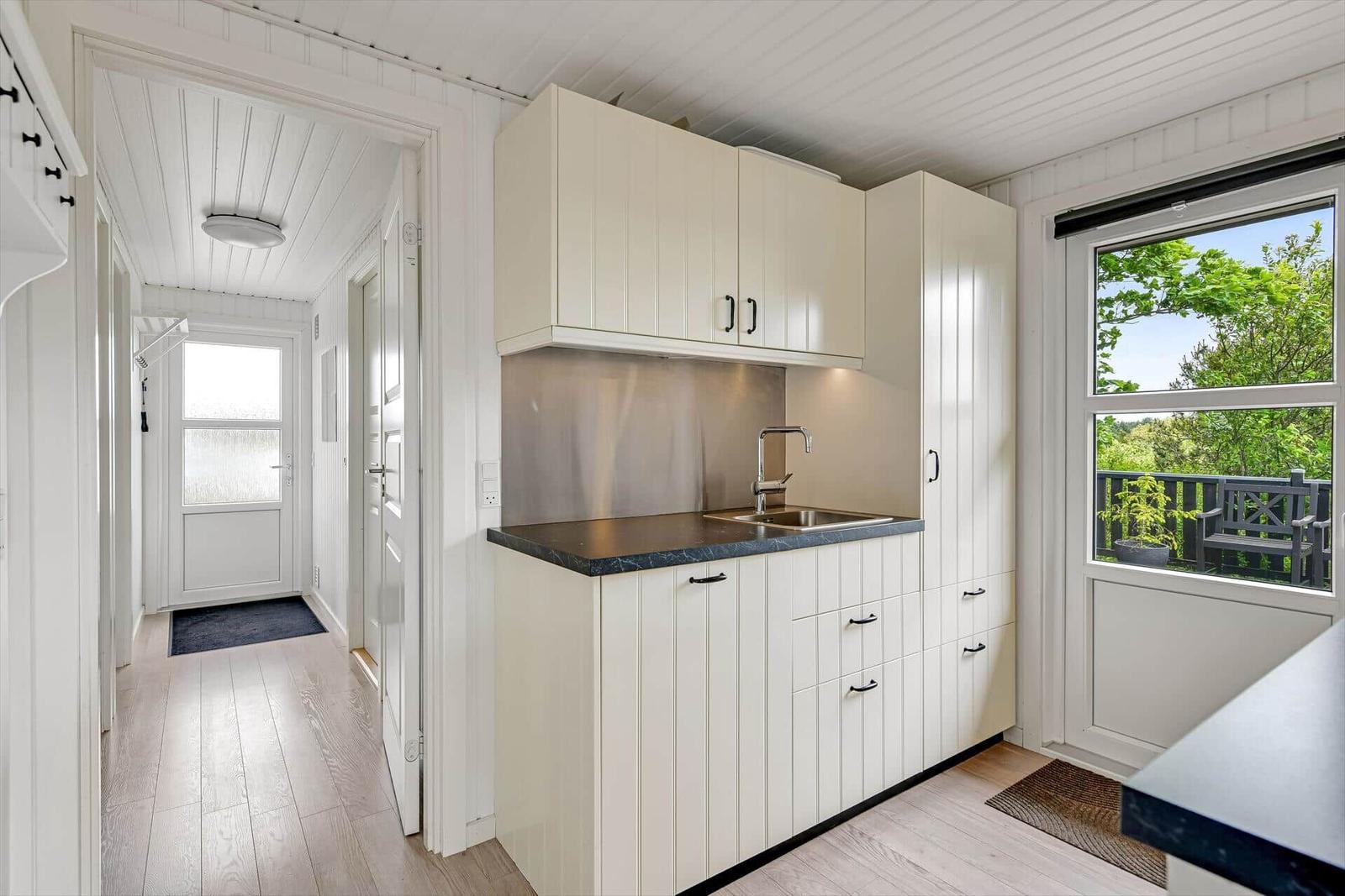 Küche mit weißen Schränken, dunklem Arbeitsplatz und Fenster zum Balkon.