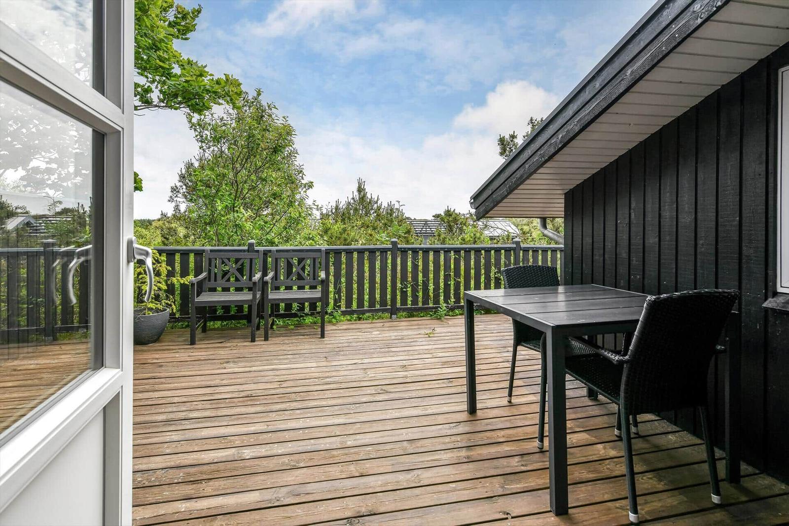 Terrasse mit Tisch, Stühlen und Blick auf grüne Bäume.