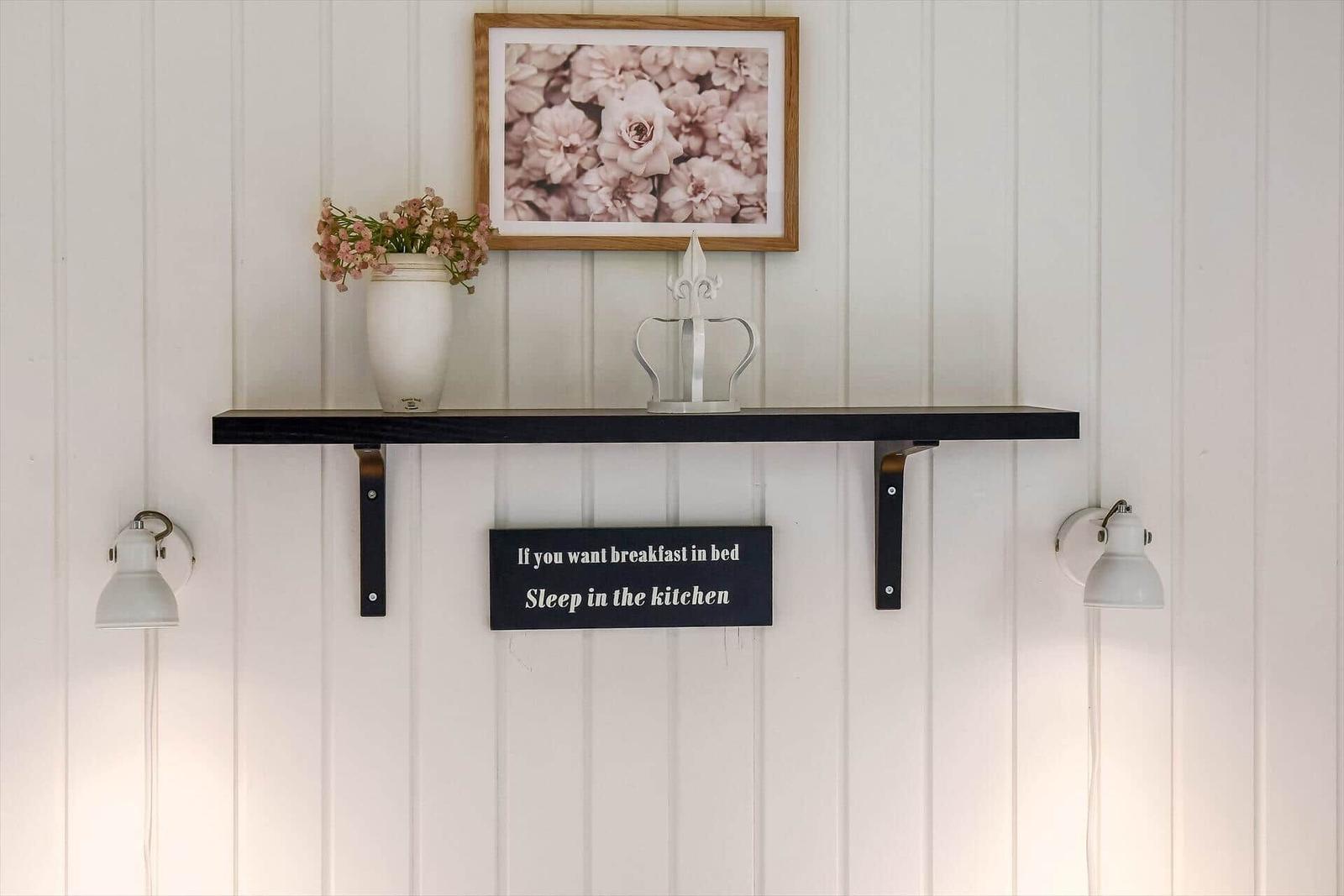 Wandregal mit Blumen, Bild und Schild über Küchenbereich.