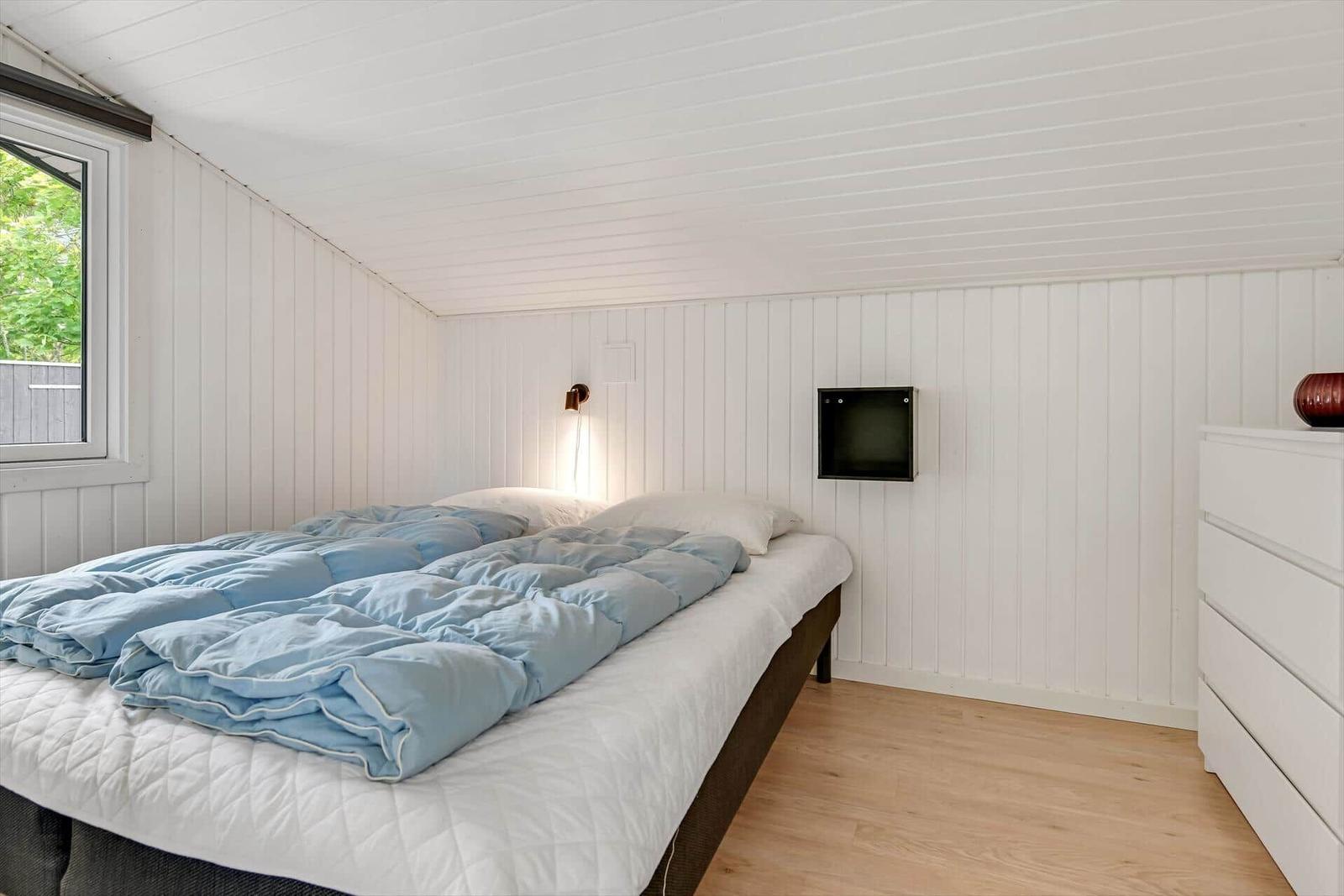 Schlafzimmer mit Bett, Fenster und Schrank. Wände und Decke sind weiß verkleidet.