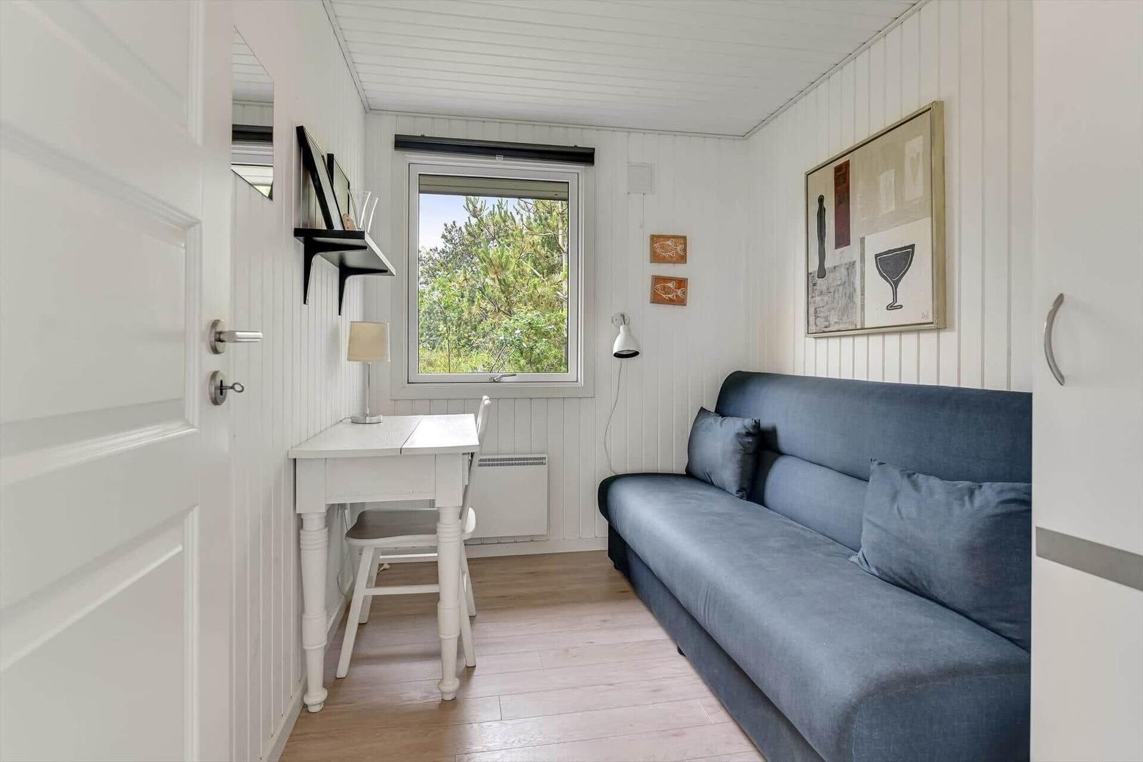Ein Raum mit Sofa, Schreibtisch und Fenster mit Blick auf Bäume.
