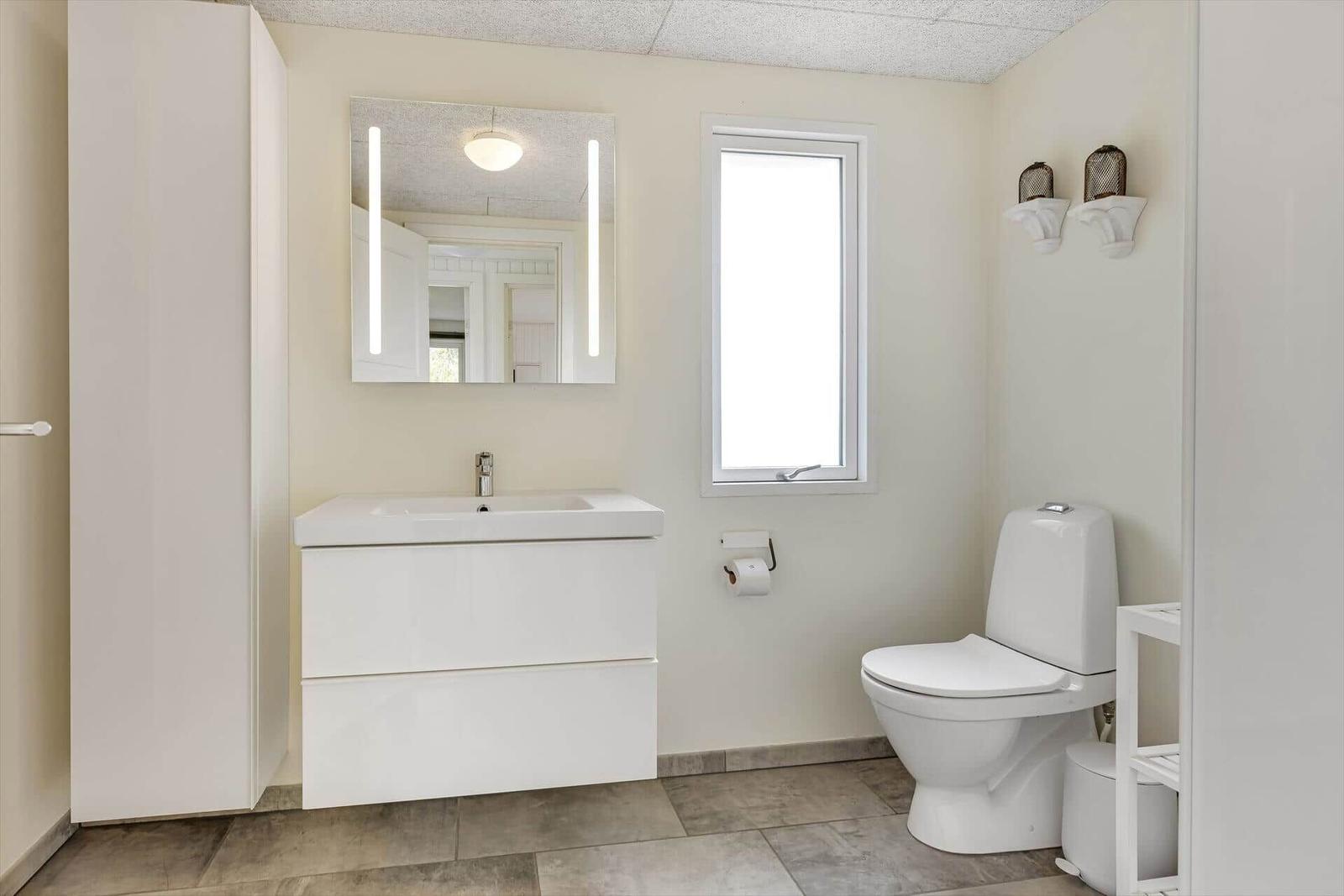 Badezimmer mit Waschbecken, Spiegel, Toilette und Fenster.