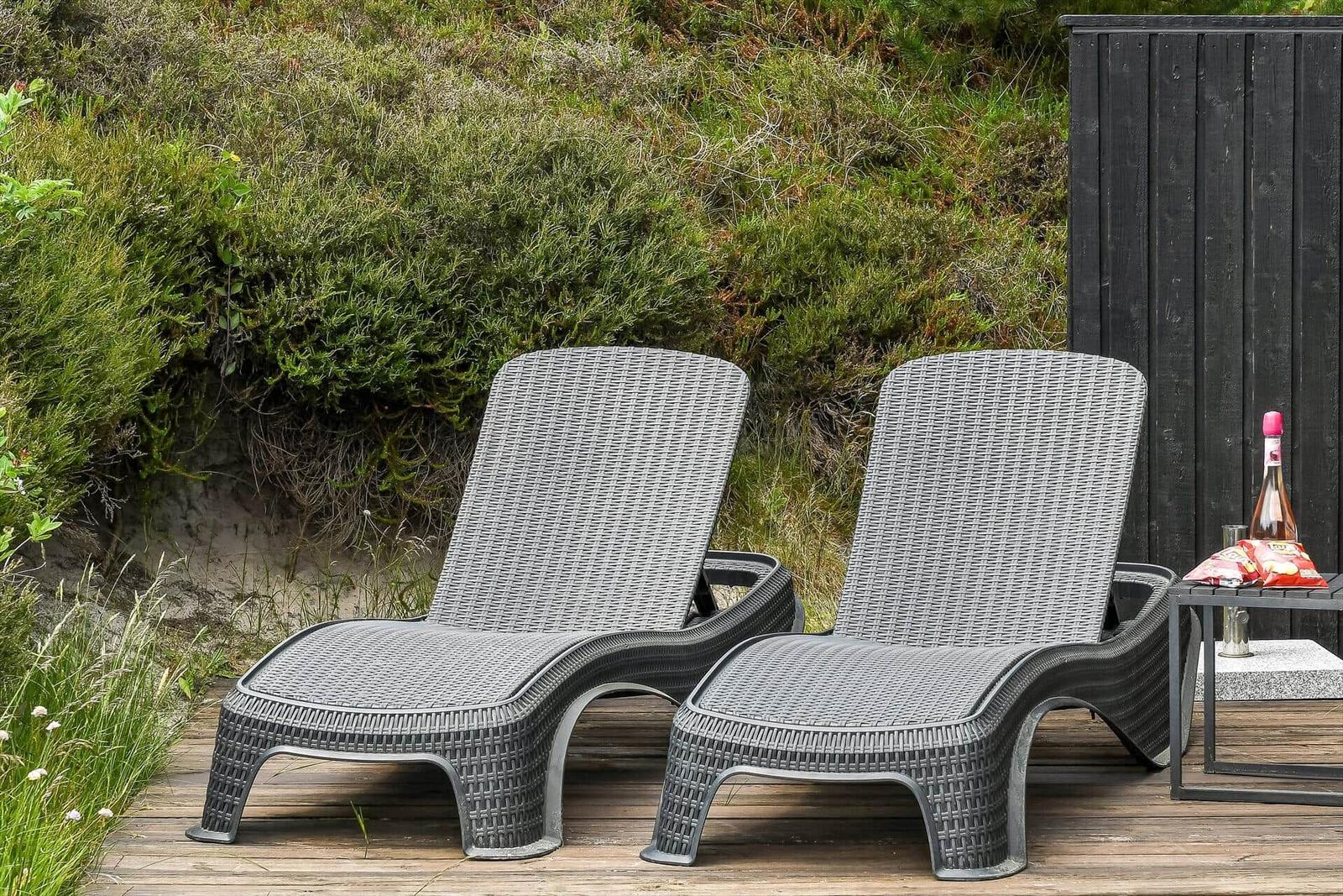 Zwei graue Rattan-Liegestühle stehen auf einer Terrasse neben einem Tisch mit Getränk.