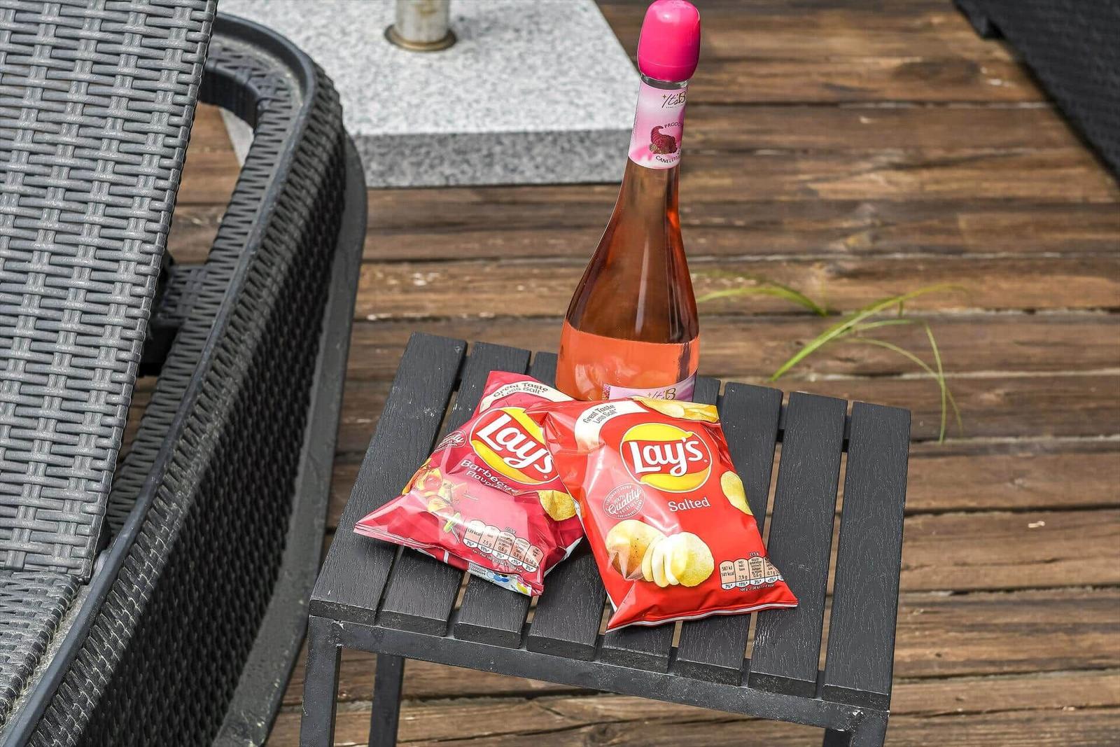 Auf einem Tisch stehen zwei Chipsbeutel und eine Flasche Sekt.