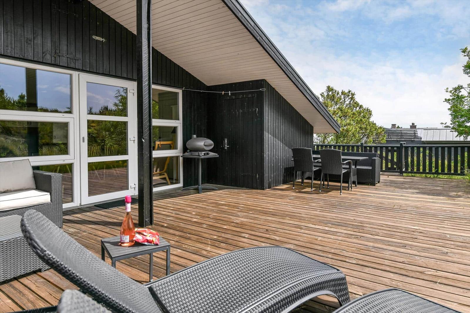 Terrasse mit Loungemöbeln, Grill und Tisch. Holzdeck und schwarze Wand.