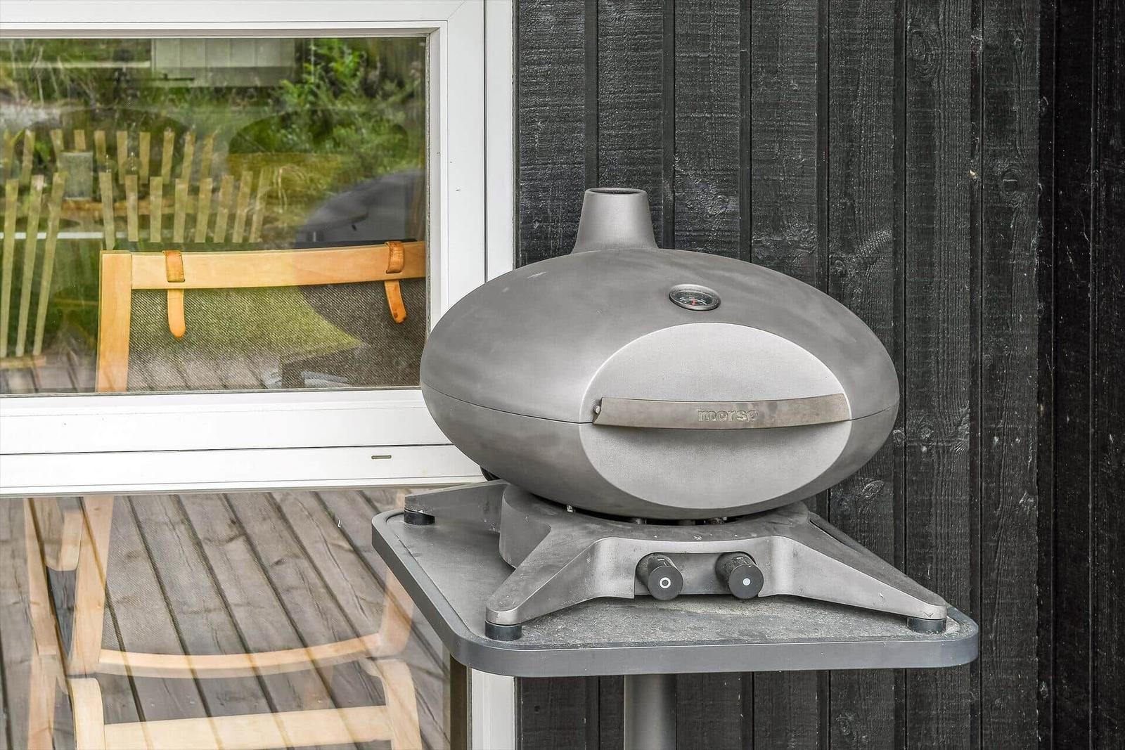 Morsy Grill auf Ständer neben Fenster mit Holzterrasse und Gartenblick.