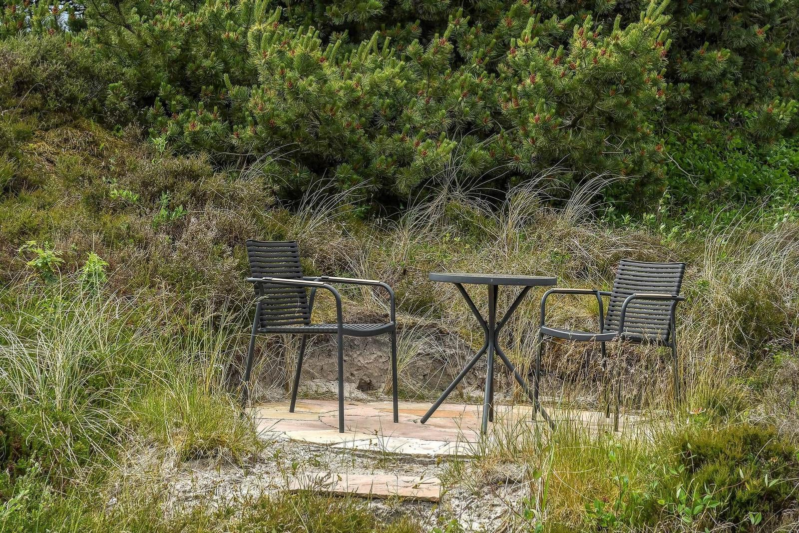 Zwei Stühle und ein Tisch stehen auf einer Steinplatte im Gras.