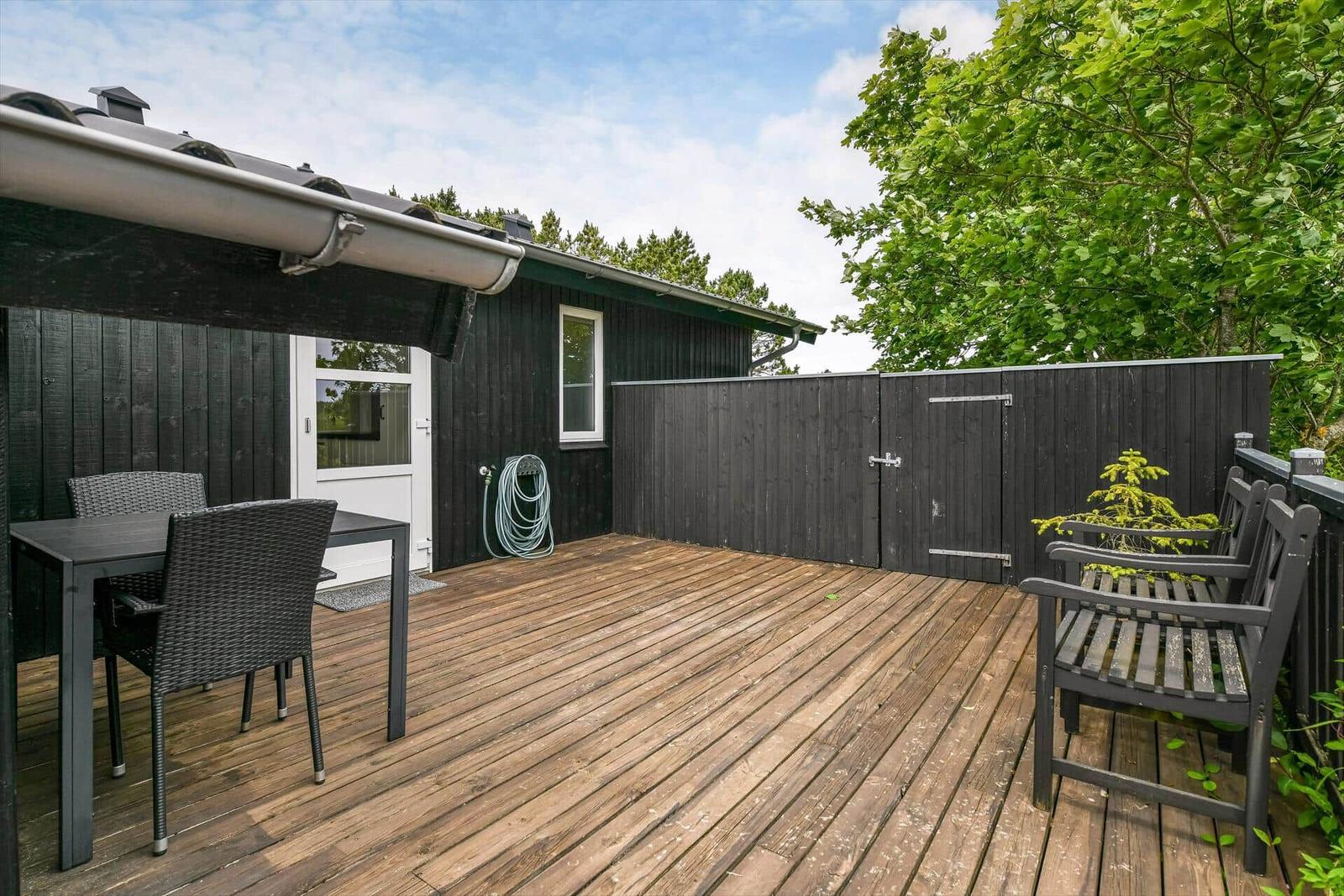 Terrasse mit Tisch, Stühlen und Sitzbank neben dunklem Holzhaus.