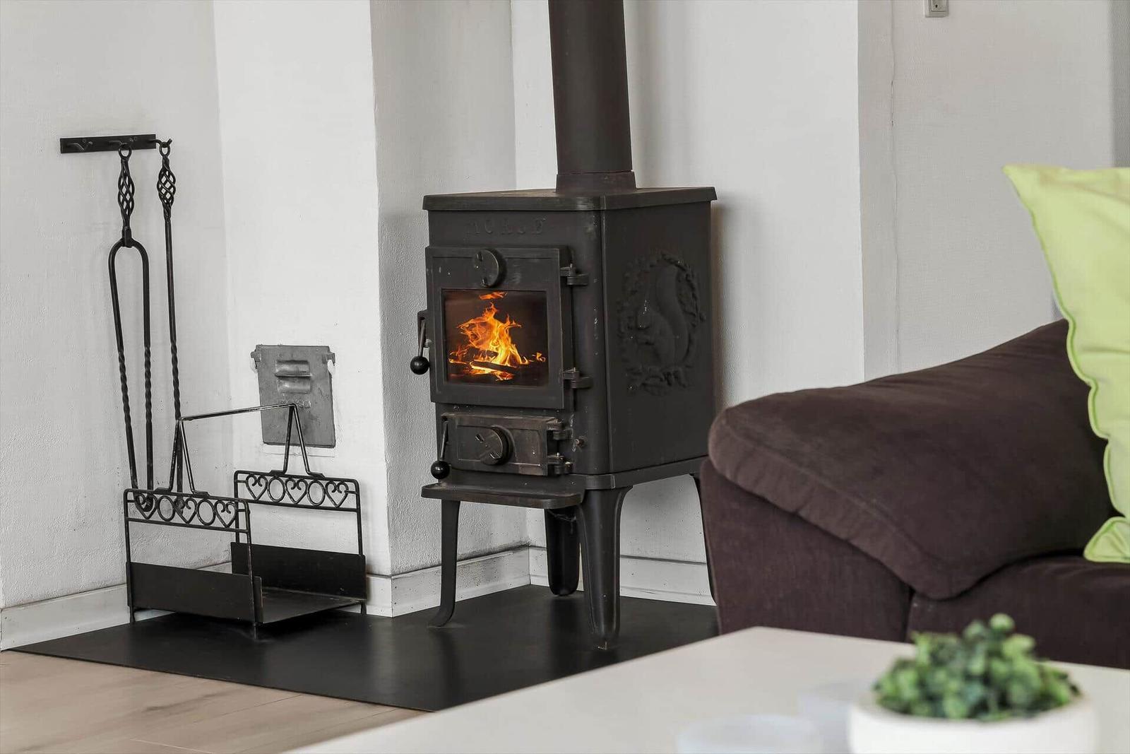 A black wood stove with burning fire is next to a sofa.