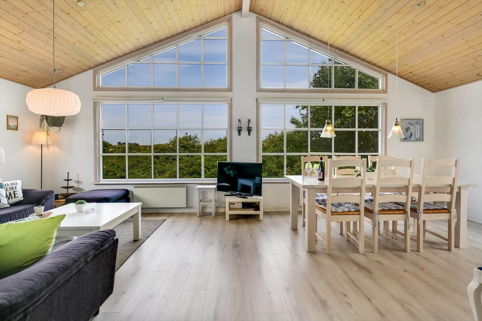 Living and dining area with large windows and wooden ceiling.