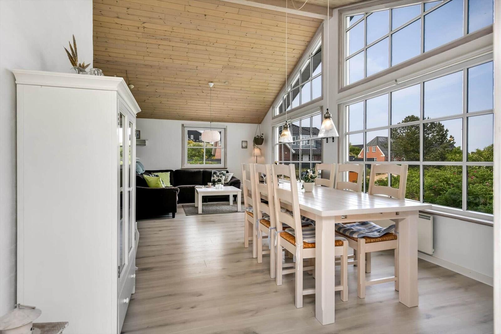 Dining room with table and chairs. Living room with sofa and coffee table. Large windows with view outside.