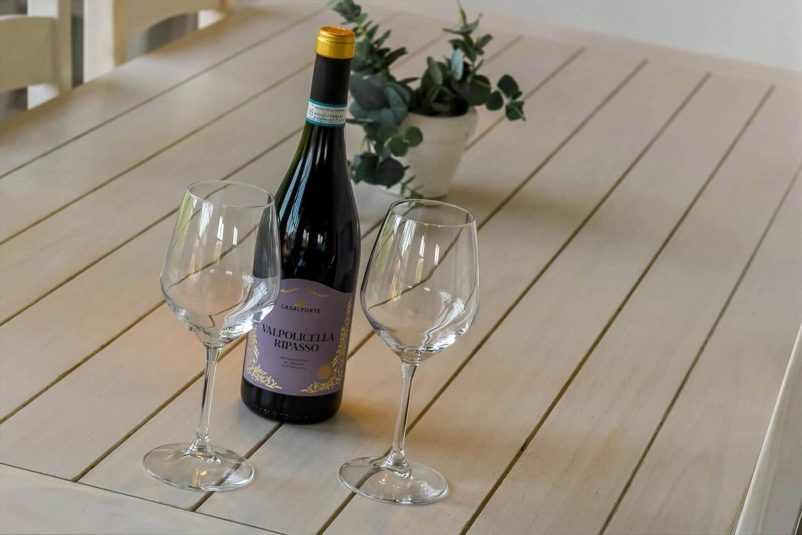 On the table, a wine bottle and two glasses sit beside a plant.