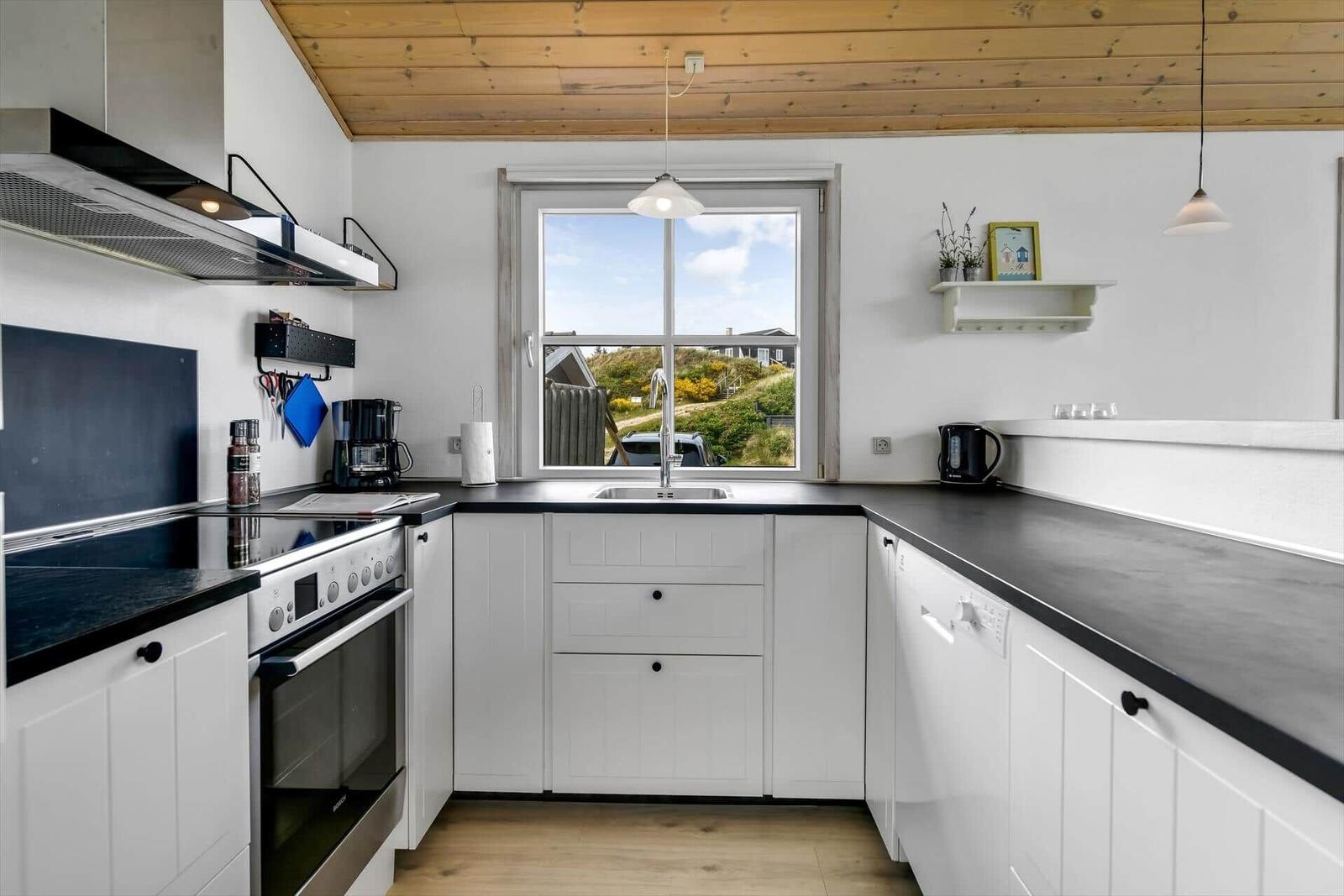 Kitchen with white cabinets, black countertops, and wooden ceiling. Window shows landscape.