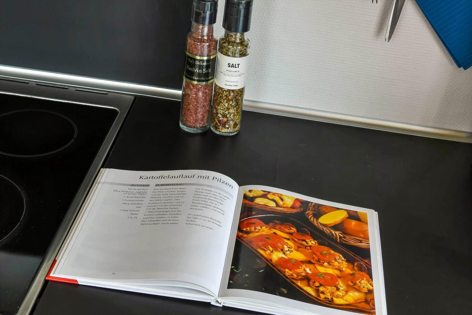 Cookbook with recipe and spice bottles on kitchen countertop.
