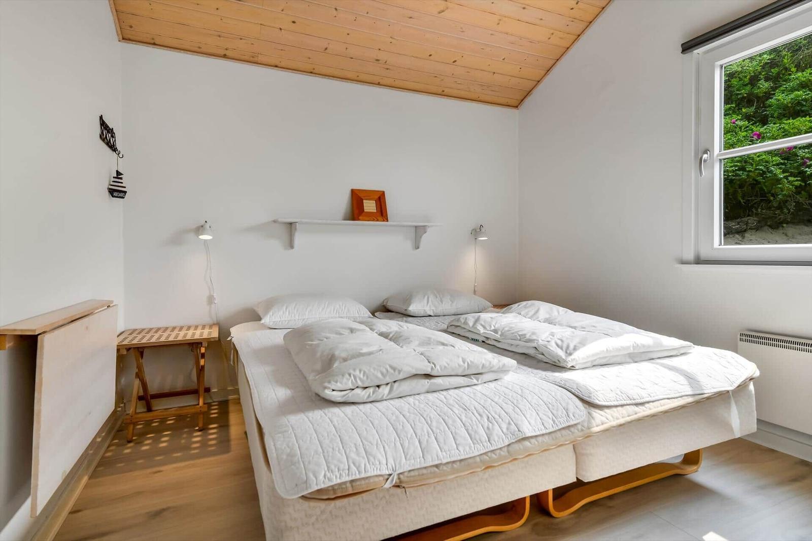 Bedroom with double bed, wooden floor, and window view of greenery.
