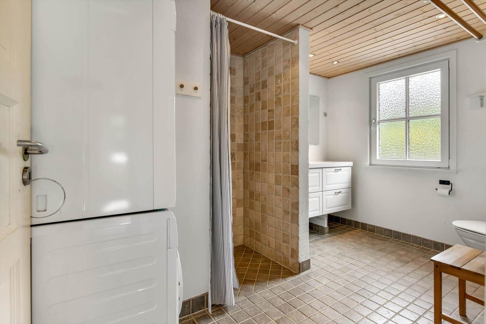 Bathroom with shower, sink, and toilet. Wooden ceiling and window with grid.