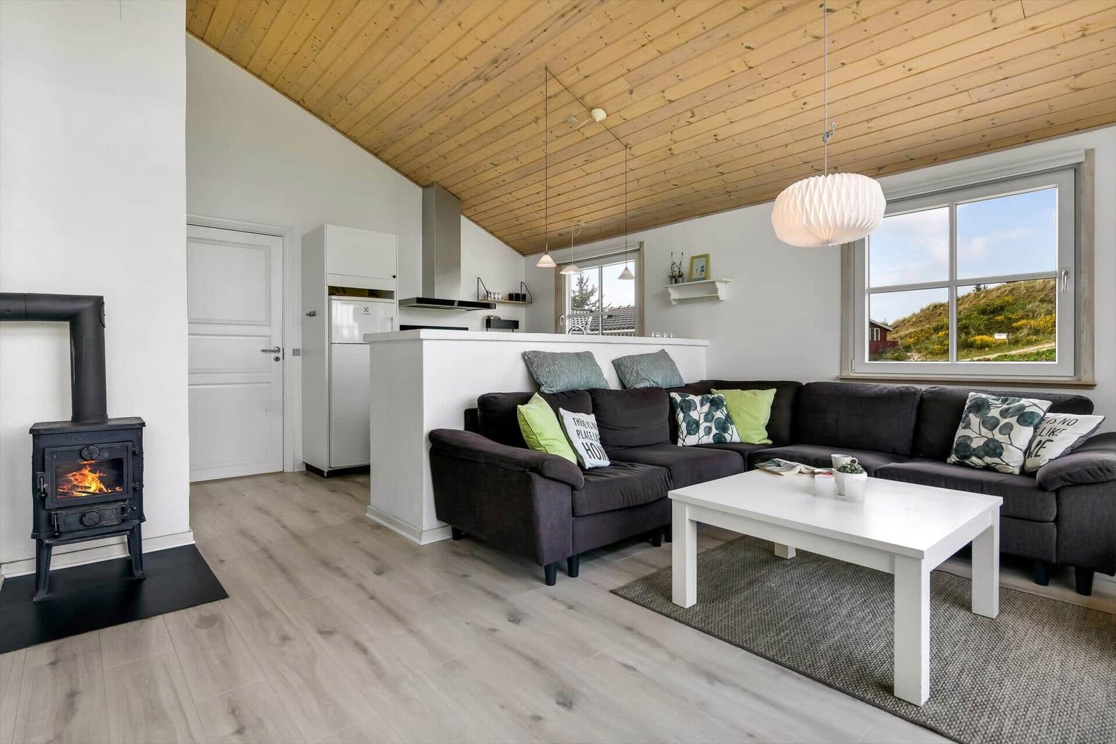 Living room with sofa, fireplace, and wooden ceiling. Kitchen in background.