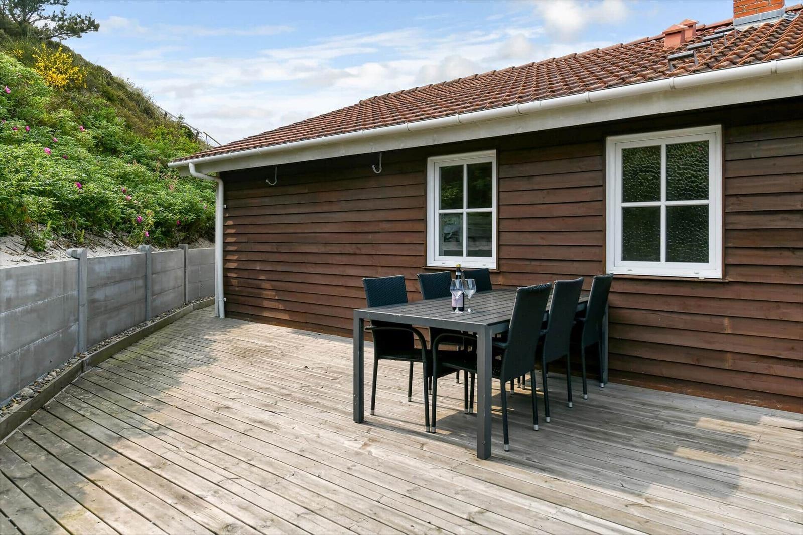 Deck with table and chairs in front of a wooden house with red roof.