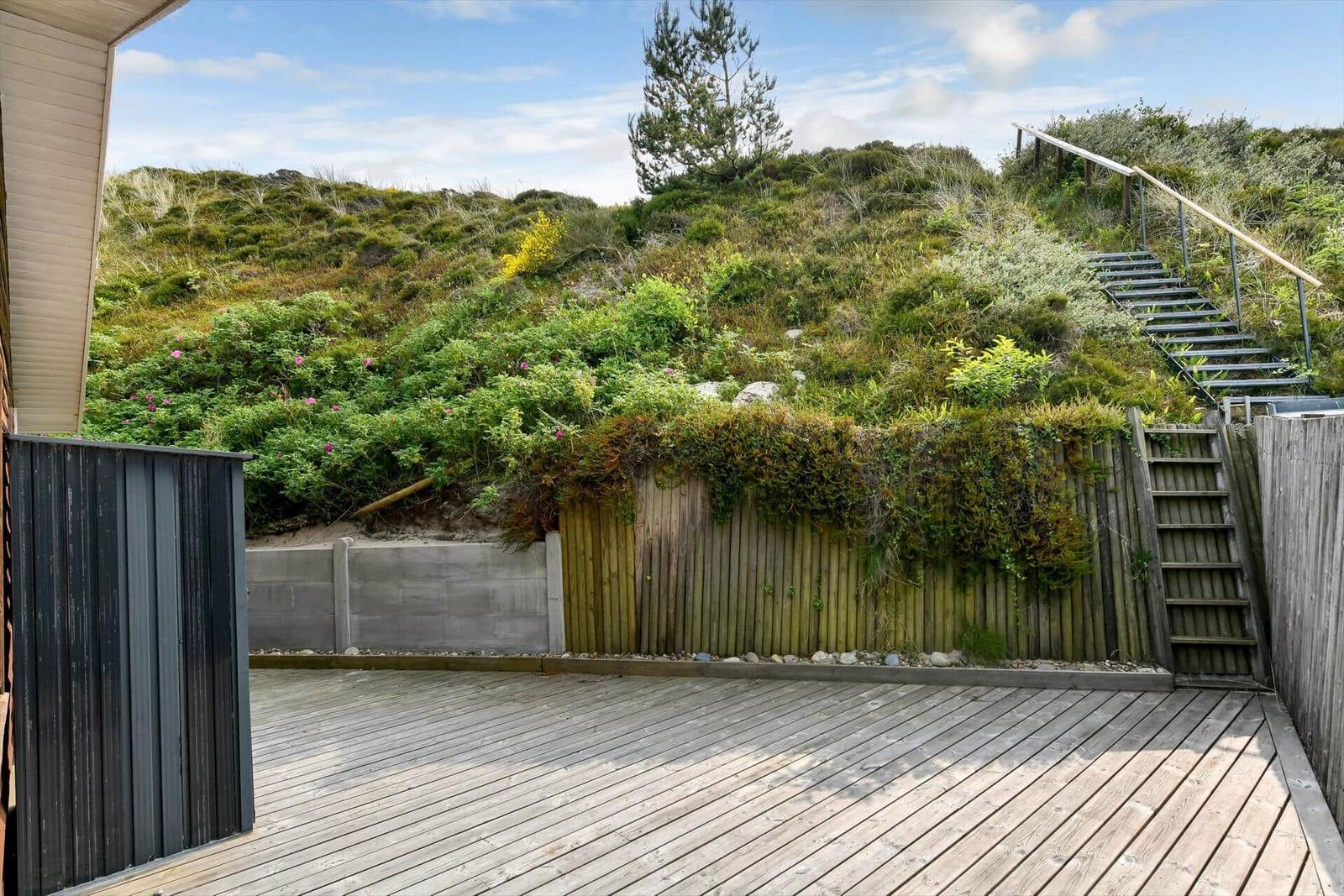 Wooden terrace with view of green dunes and staircase.