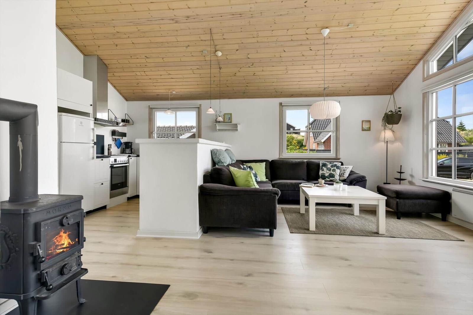 Living and kitchen area with wooden ceiling, fireplace, and large windows.