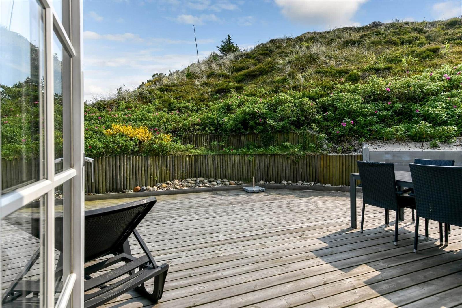 Deck with lounge chair and table, view of green slopes with flowers.